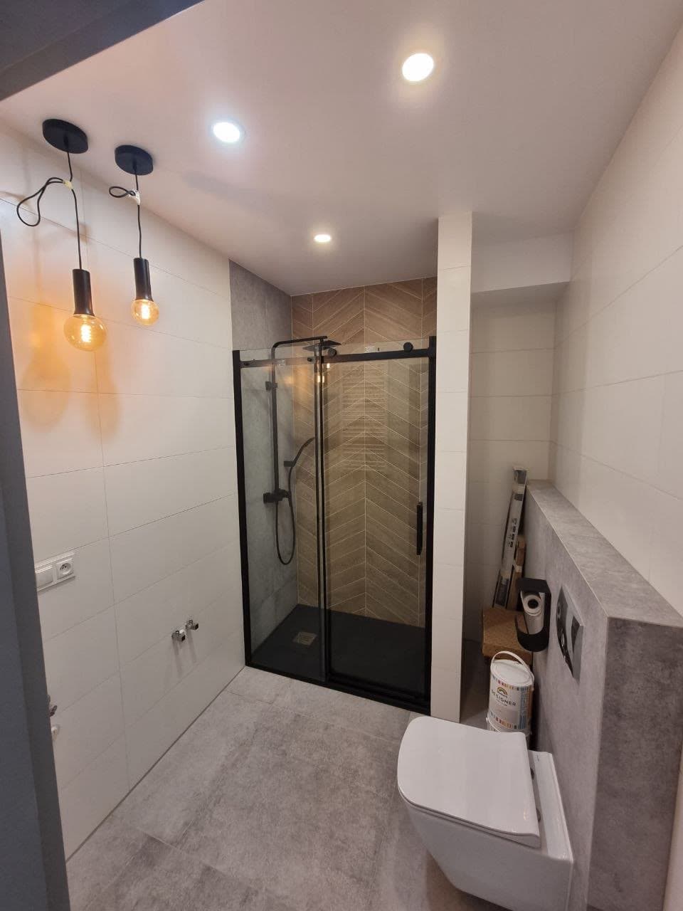 Finished walk-in glass shower with black fixtures and pendant lighting
