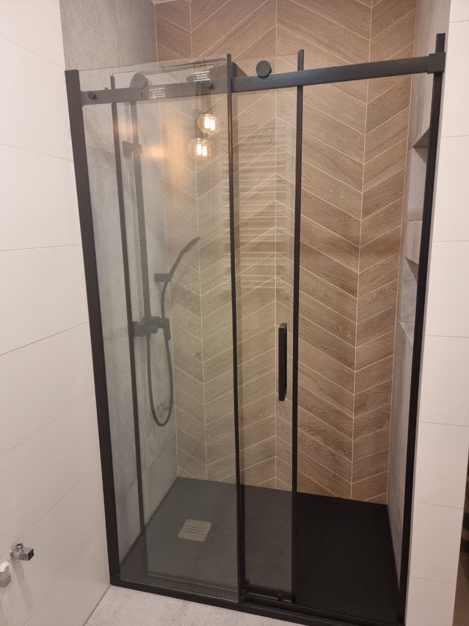 Finished walk-in shower with a black-framed sliding glass door and herringbone tile