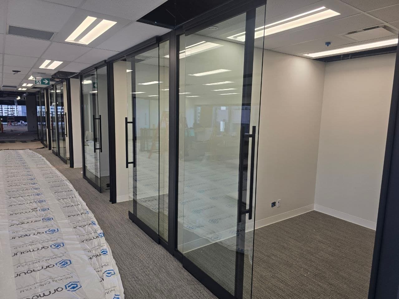 Bright run of black-framed glass partition offices along a finished corridor