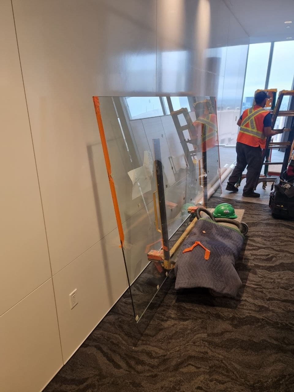 Installer in safety gear setting a large glass partition panel on a Calgary office floor