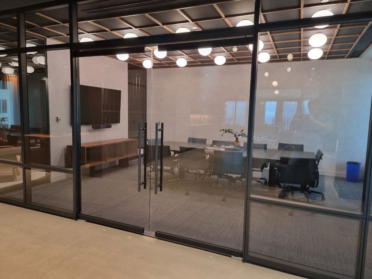 Finished black-framed glass boardroom with a wood-grid ceiling and globe lighting
