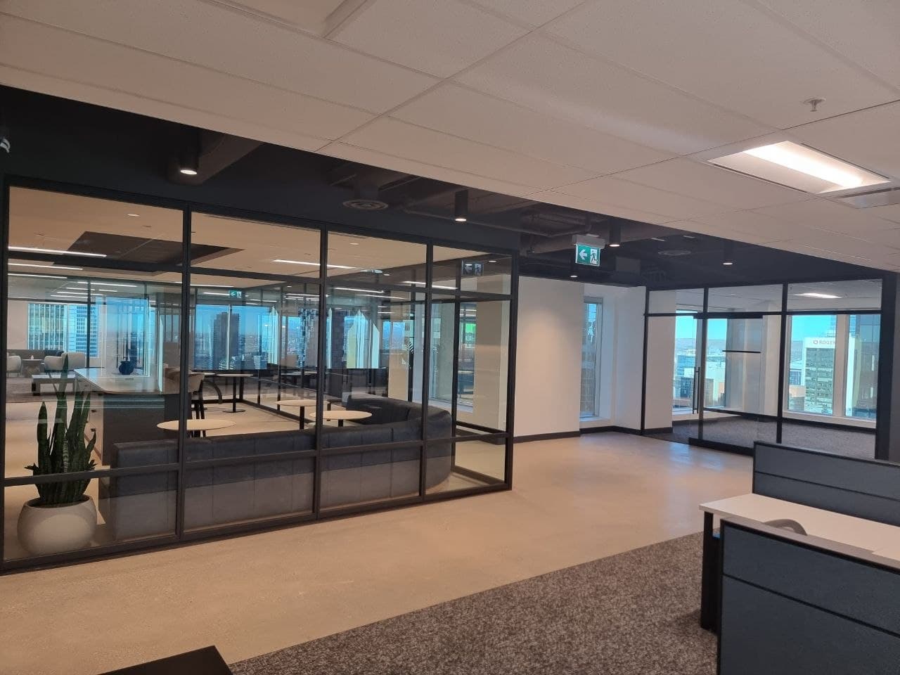 Curved black-framed glass partition around a lounge with downtown Calgary views
