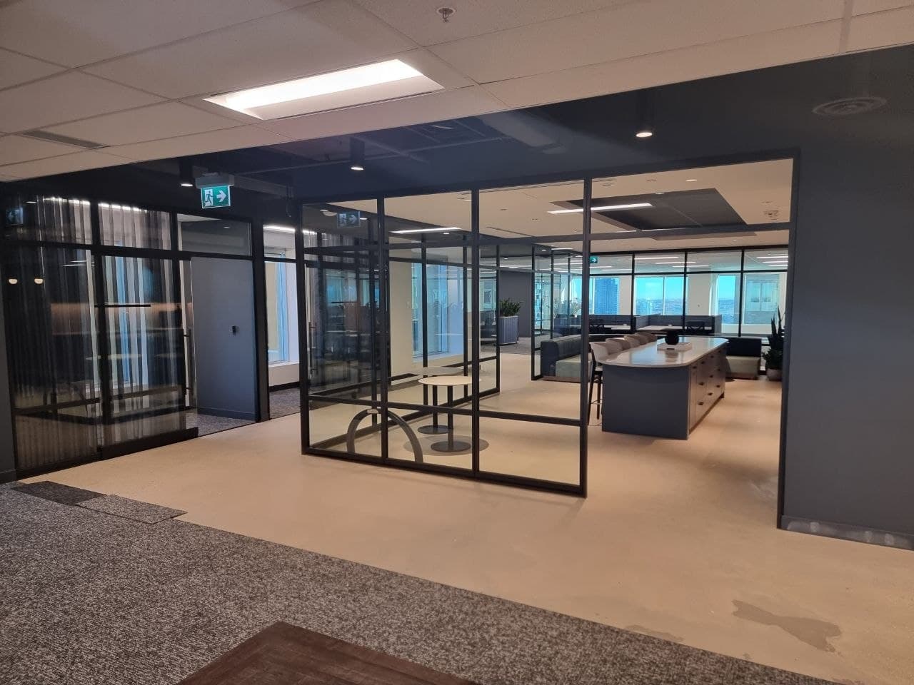 Black-framed glass meeting room beside an open kitchen island with city views — Calgary