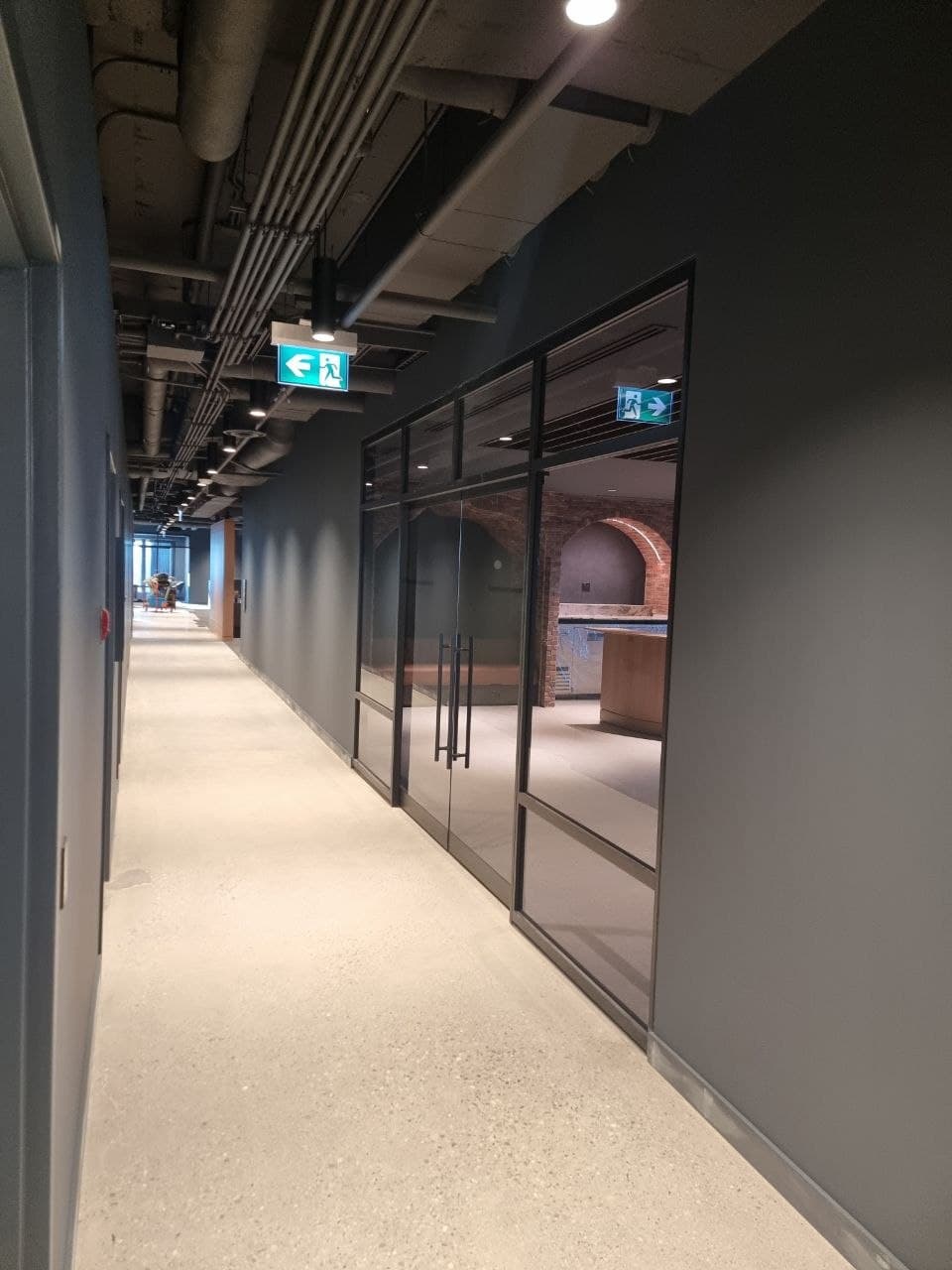 Black-framed glass doors opening to a lounge with exposed-brick detailing — Calgary office fit-out