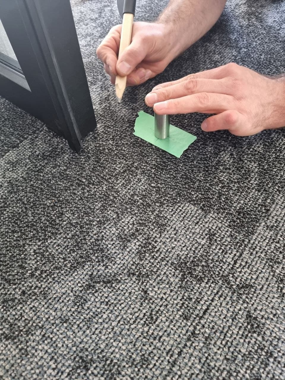 Marking a floor anchor point by hand with a pencil before drilling for a glass partition track — Calgary install