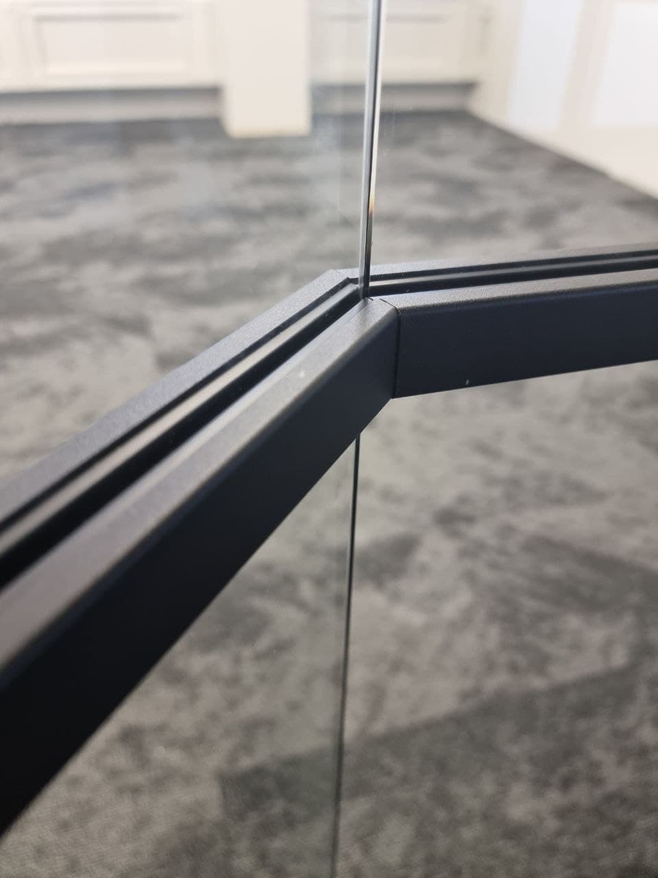 Close-up of a precisely mitred black frame joint where two glass partition panels meet