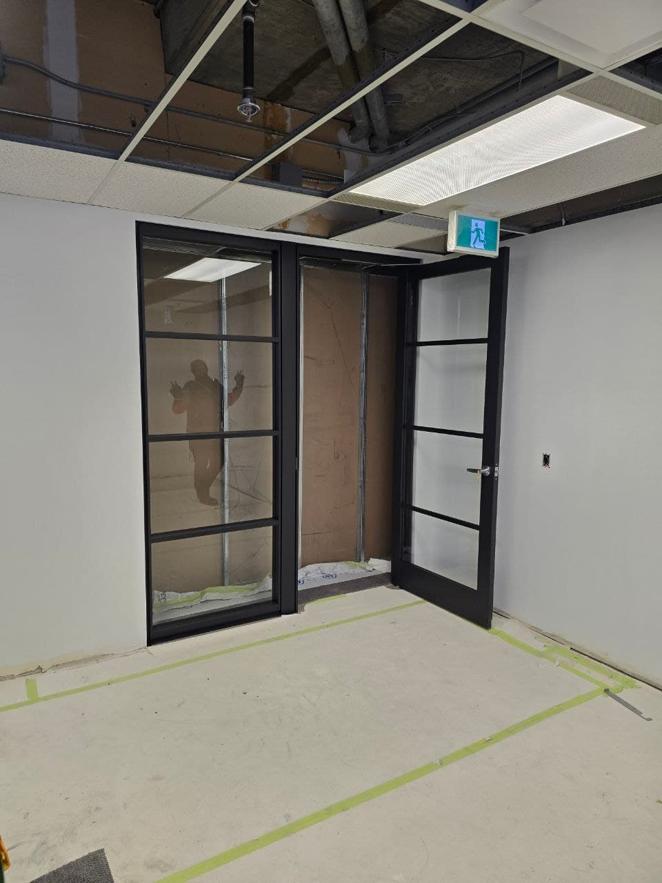 Newly installed black-framed glass office door, open beside the exit sign — Calgary door installation
